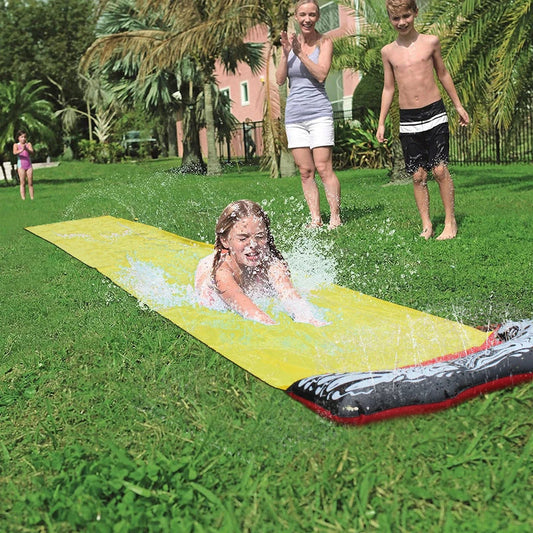 Children playing on a yellow inflatable water slide in a backyard garden