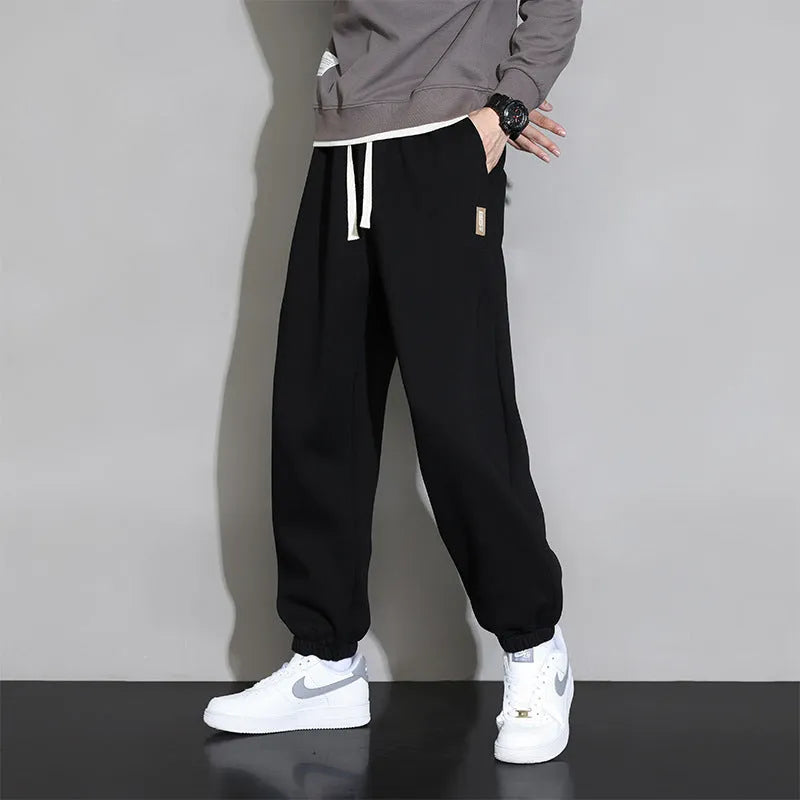 Man wearing loose grey sports trousers with an elasticated drawstring waistband.