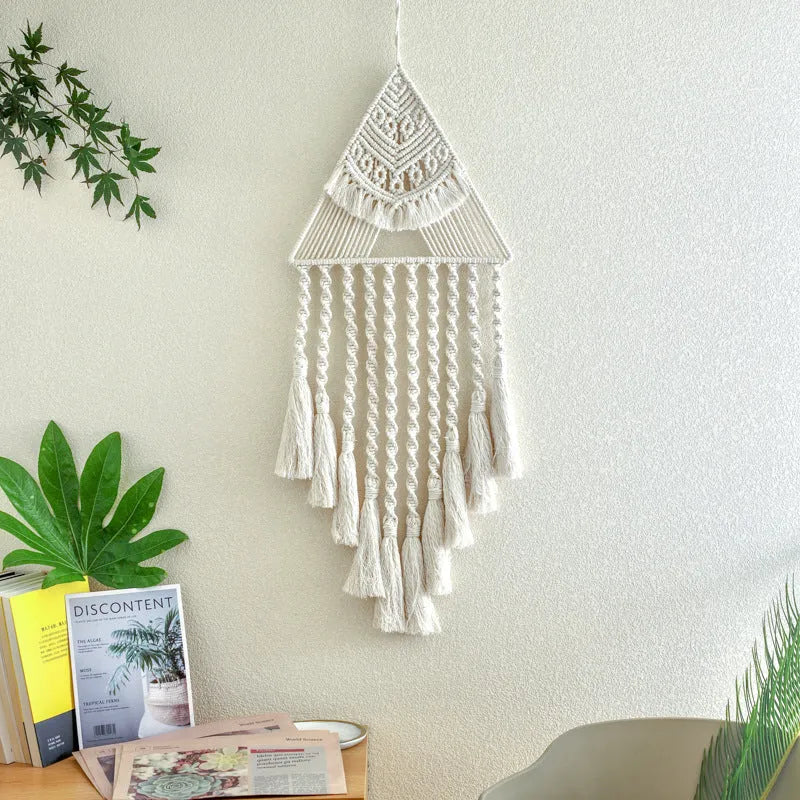 Large white handwoven triangle dream catcher pendant with wooden beads and a long tassel hanging on a wall.