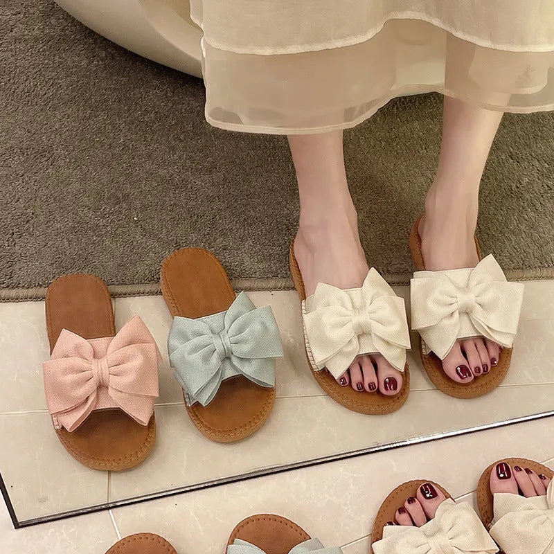 Women's beige suede slip-on sandals with a bow detail and soft rubber flat sole.