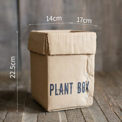 A grey cement flowerpot with a folded paper box design, shown with a drainage hole in its base.