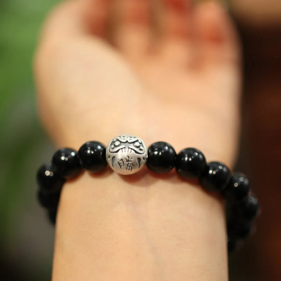 Close-up of a women's black agate bracelet with 10mm beads and a sterling silver clasp on a wrist.