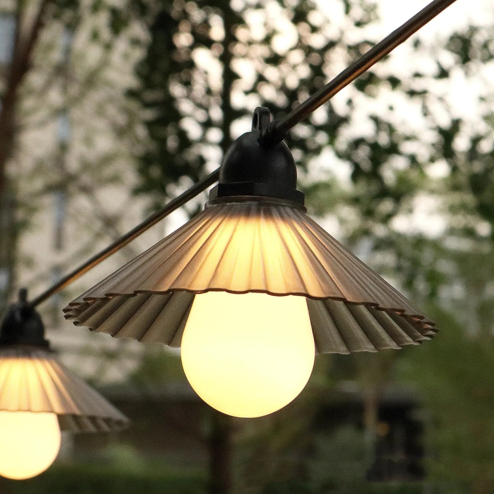 Outdoor LED string lights with white flower-shaped globes, shown illuminating a garden patio at dusk.