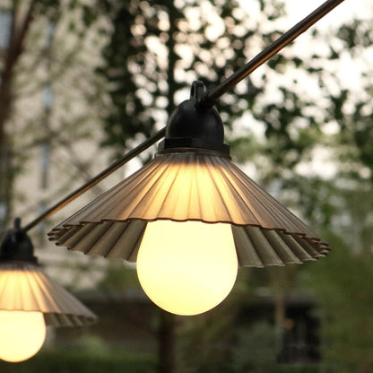 Outdoor LED string lights with white flower-shaped globes, shown illuminating a garden patio at dusk.