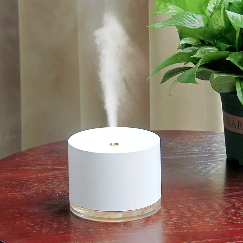 White portable ultrasonic humidifier with LED light and USB charging port on a wooden surface.
