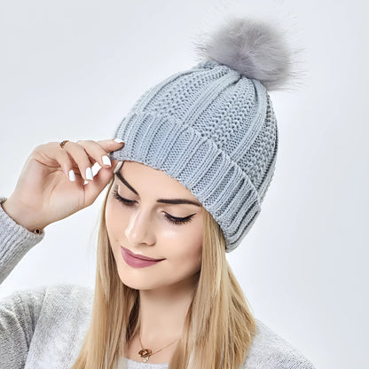 Woman wearing a wine red wool beanie hat with a faux fur pom pom and satin lining.