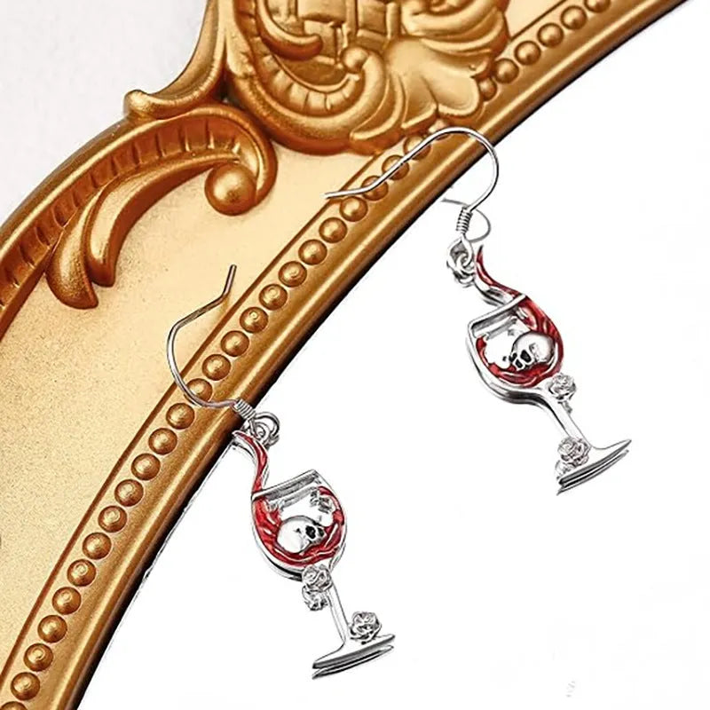 Close-up of a pair of silver-toned geometric earrings combining a skull motif with a wine glass shape.