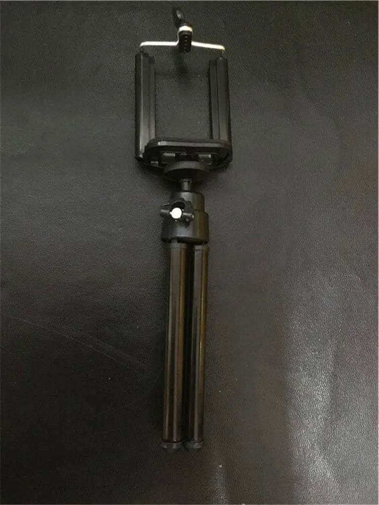 Black adjustable desktop phone holder with extended arm on a wooden desk, holding a mobile phone.