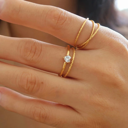 A gold-coloured stainless steel ring in a heart shape and an oval shape on a simple band.