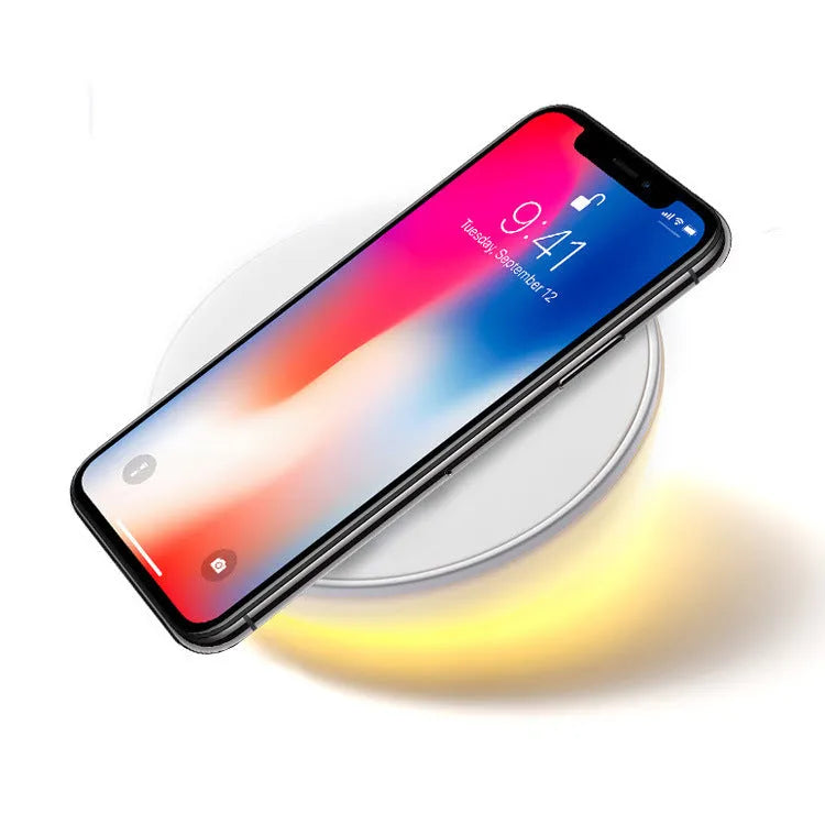 White wireless charging pad with digital clock display and three control buttons on a bedside table.