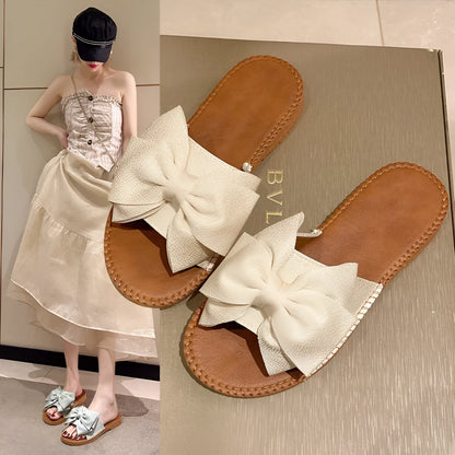 Women's beige suede slip-on sandals with a bow detail and soft rubber flat sole.