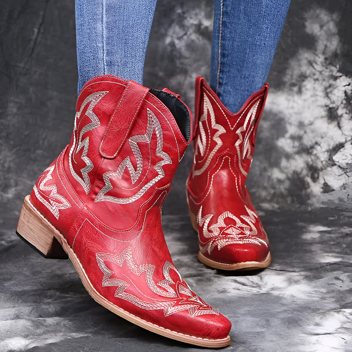 Blue women's cowboy ankle boots with embroidery and a low wedge heel on a wooden floor.