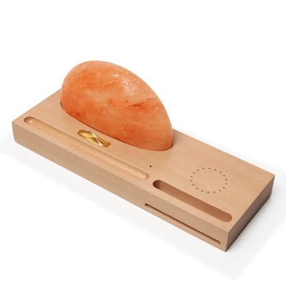 Natural crystal salt lamp with wooden base on a table, wirelessly charging a smartphone.