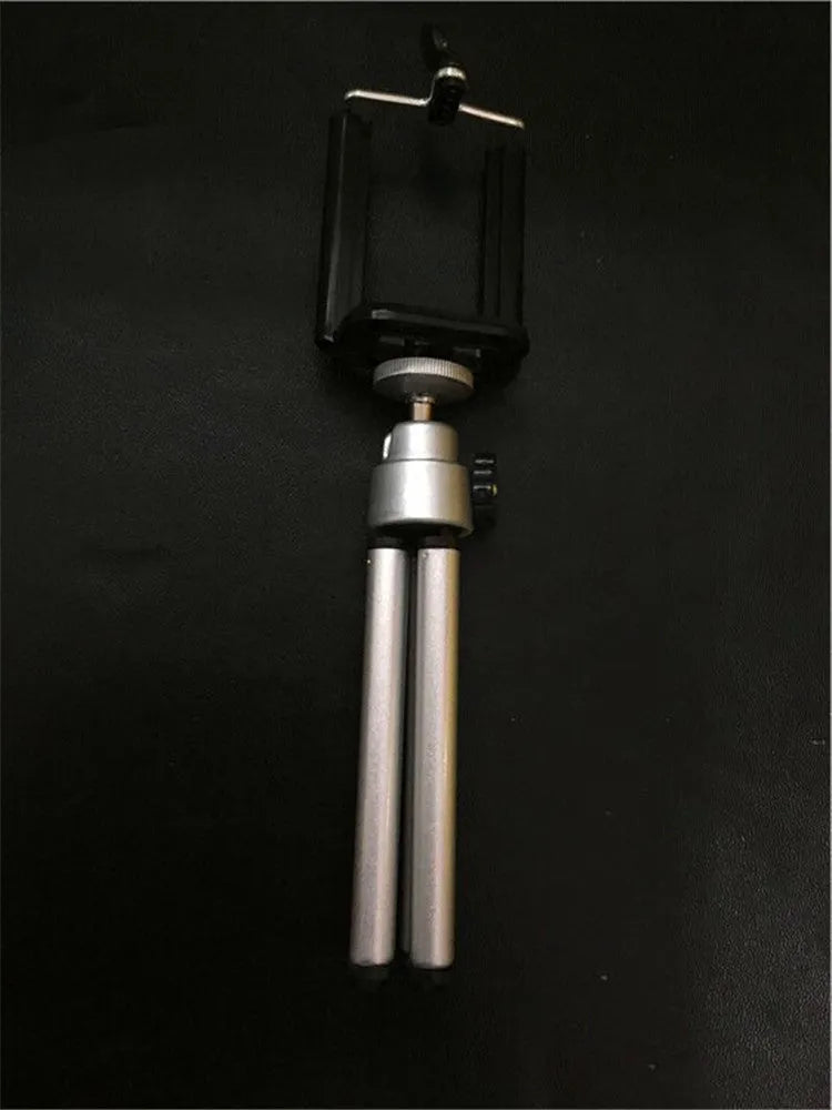 Black adjustable desktop phone holder with extended arm on a wooden desk, holding a mobile phone.