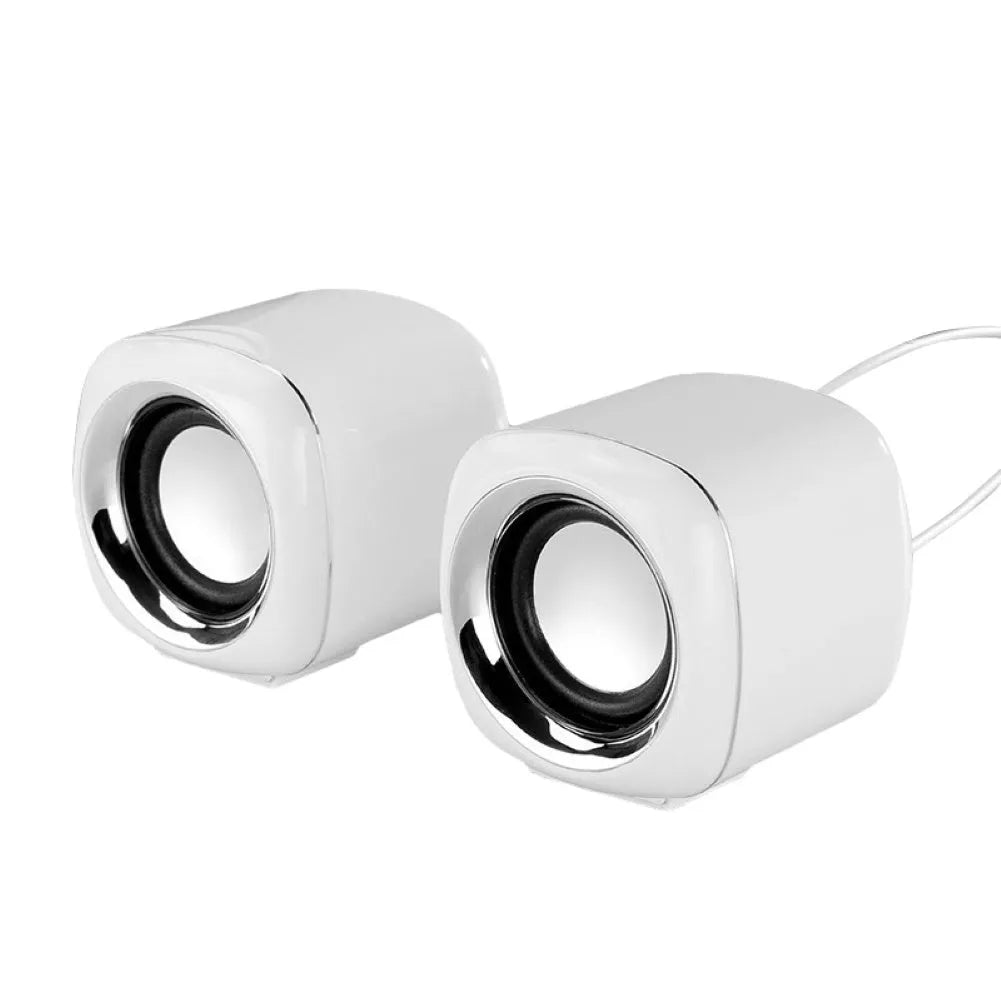 A pair of small black or white cube-shaped wired computer speakers with a 3.5mm audio plug on a desk.