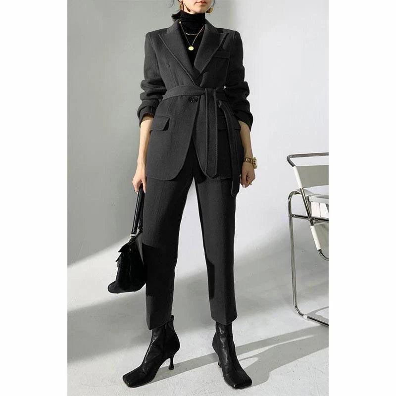 A chic and elegant woolen pant suit in black, featuring a belted jacket and warm trousers perfect for the autumn-winter season.