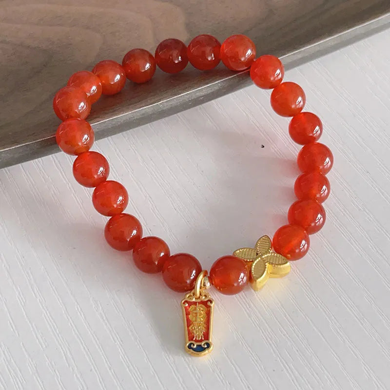 Close-up of a red agate bracelet with a dragon charm and Lucky Bag symbol on a wrist.