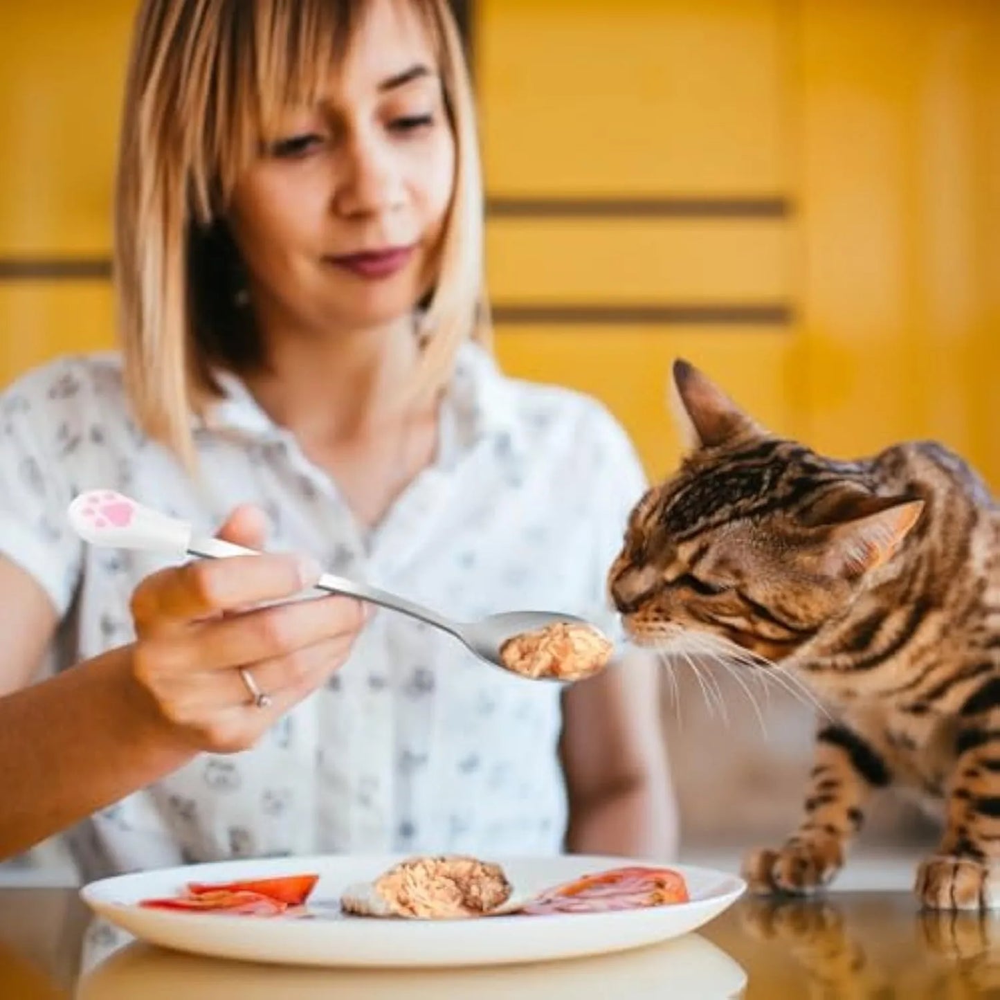 Two pet food spoons with cat paw designs - one white and one black with stainless steel and silicone construction