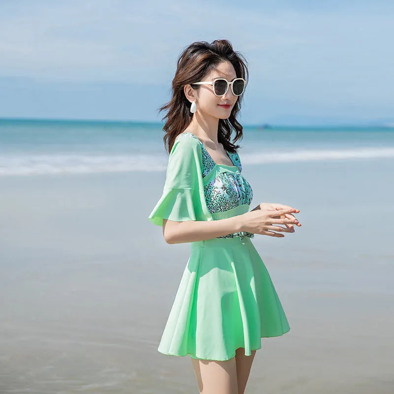 Women's green and blue seaside print one-piece swimsuit on hanger.