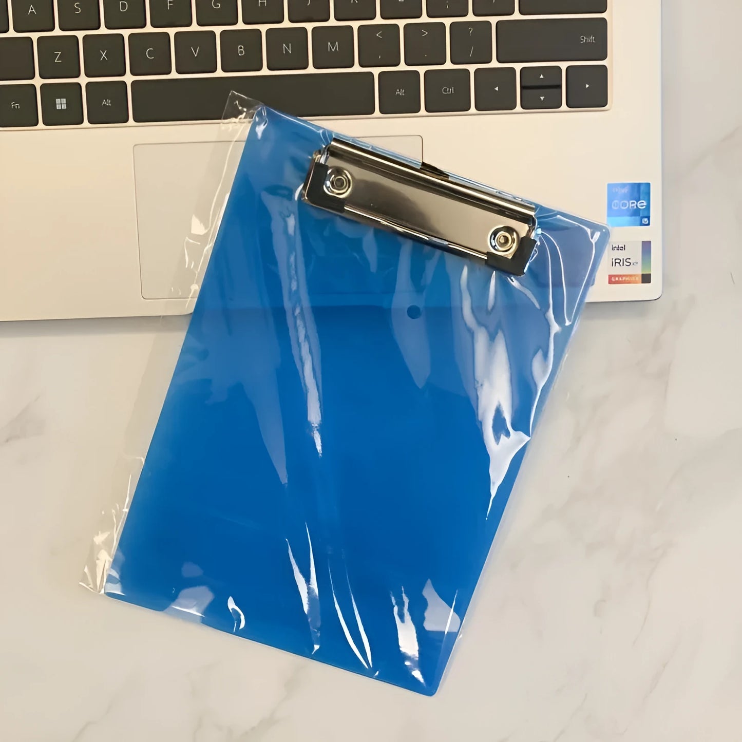 Transparent A4 plastic plate holder with metal clip, holding white paper, on a desk.