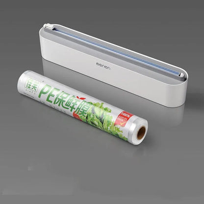 Black plastic cling film cutter and dispenser unit mounted on a refrigerator door.