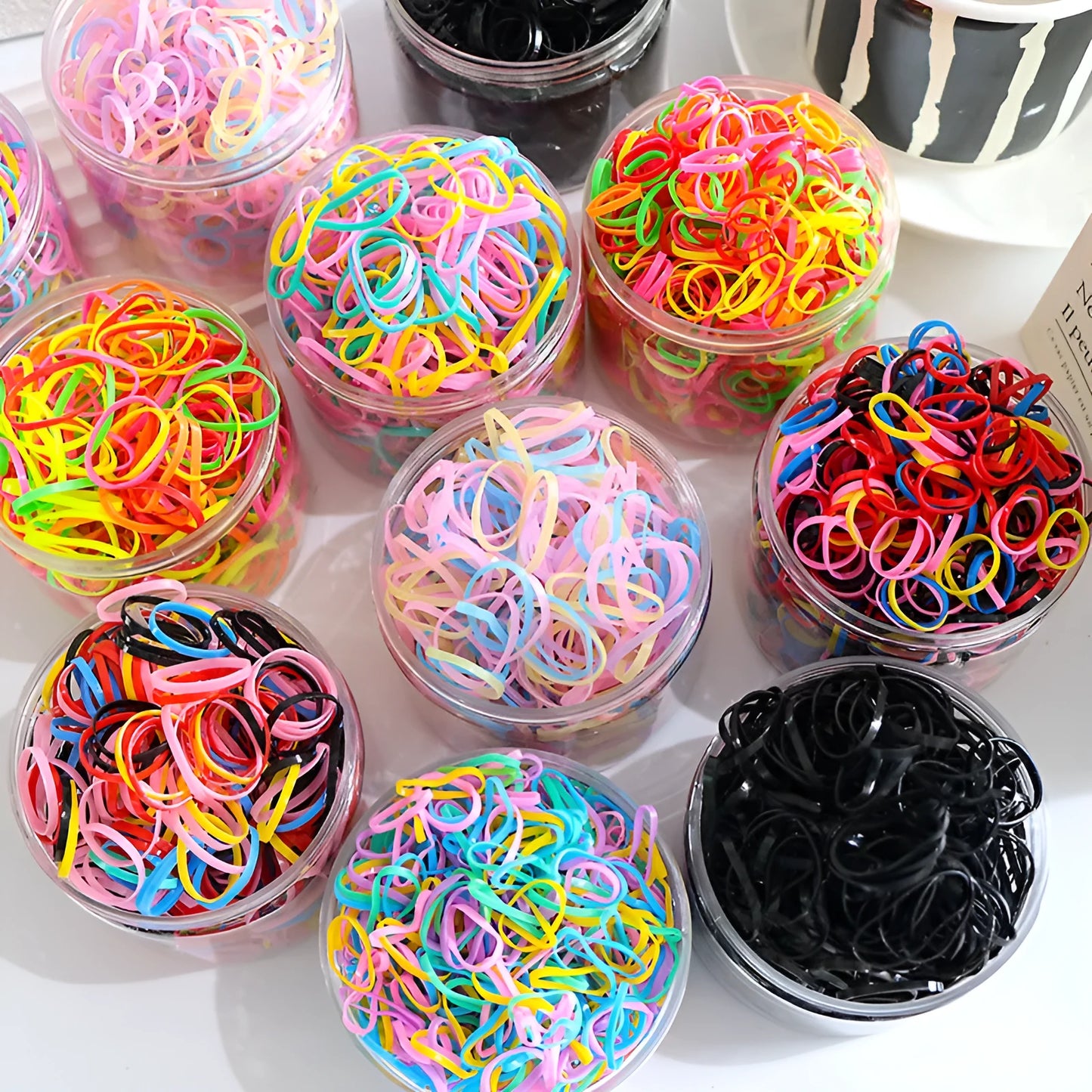 Assorted colourful thin TPU baby hair ties for toddlers and kids in a reusable plastic storage container.