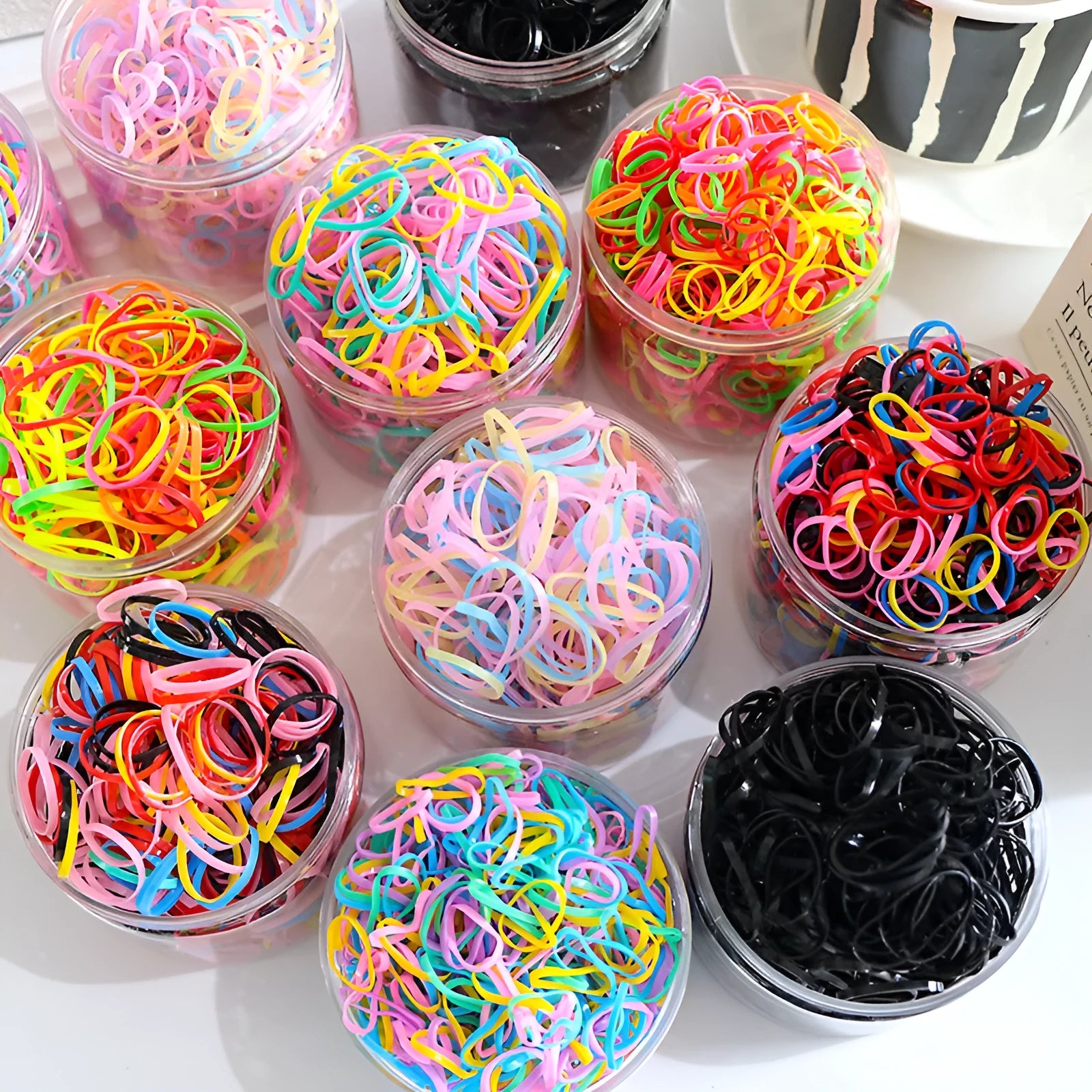 Assorted colourful thin TPU baby hair ties for toddlers and kids in a reusable plastic storage container.