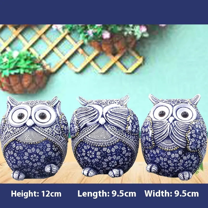 Three blue and white owl resin ornaments with hand-painted pastoral design on wooden surface
