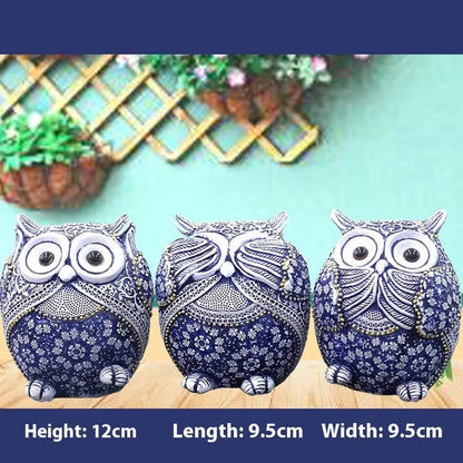 Three blue and white owl resin ornaments with hand-painted pastoral design on wooden surface