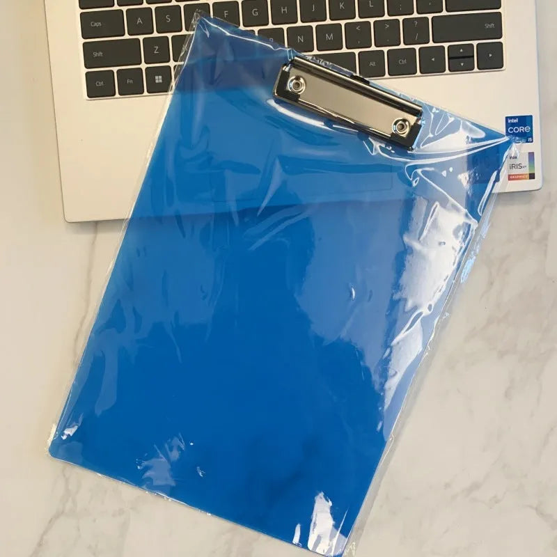 Transparent A4 plastic plate holder with metal clip, holding white paper, on a desk.