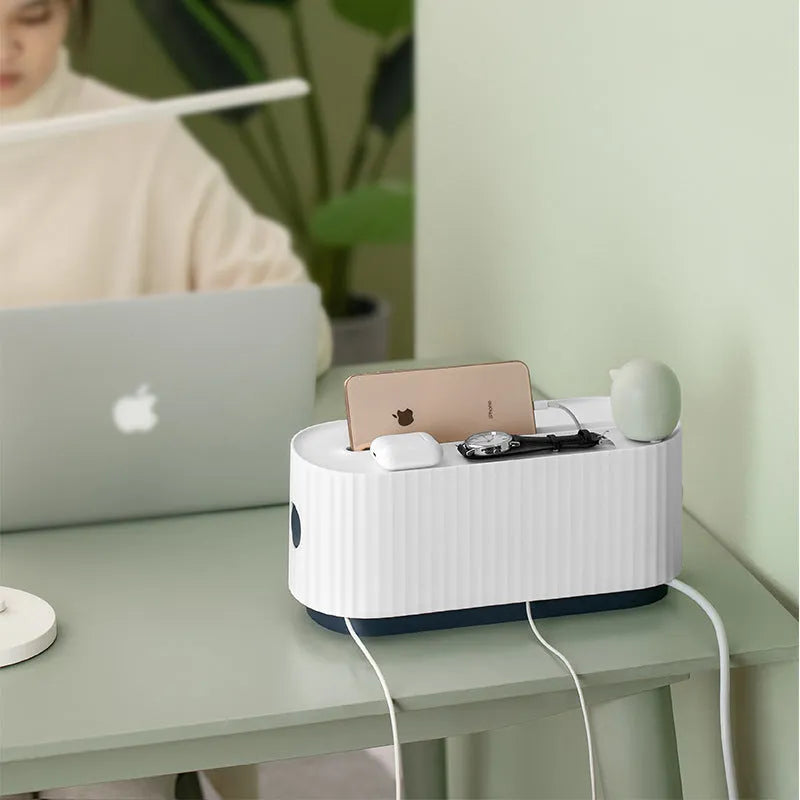 Blue desktop cable storage box with a white lid, showing cable ports on the base and a mobile phone sitting in its slot on top.
