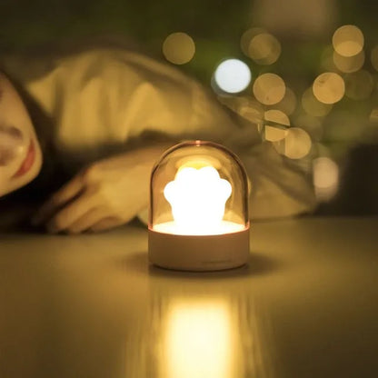 Grey cat paw night light with USB cable on a wooden desk, showing soft glow and detailed paw sculpt.