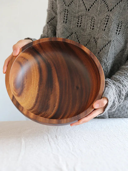 Set of five brown wooden bowls in different sizes on a wooden table, showing natural grain.