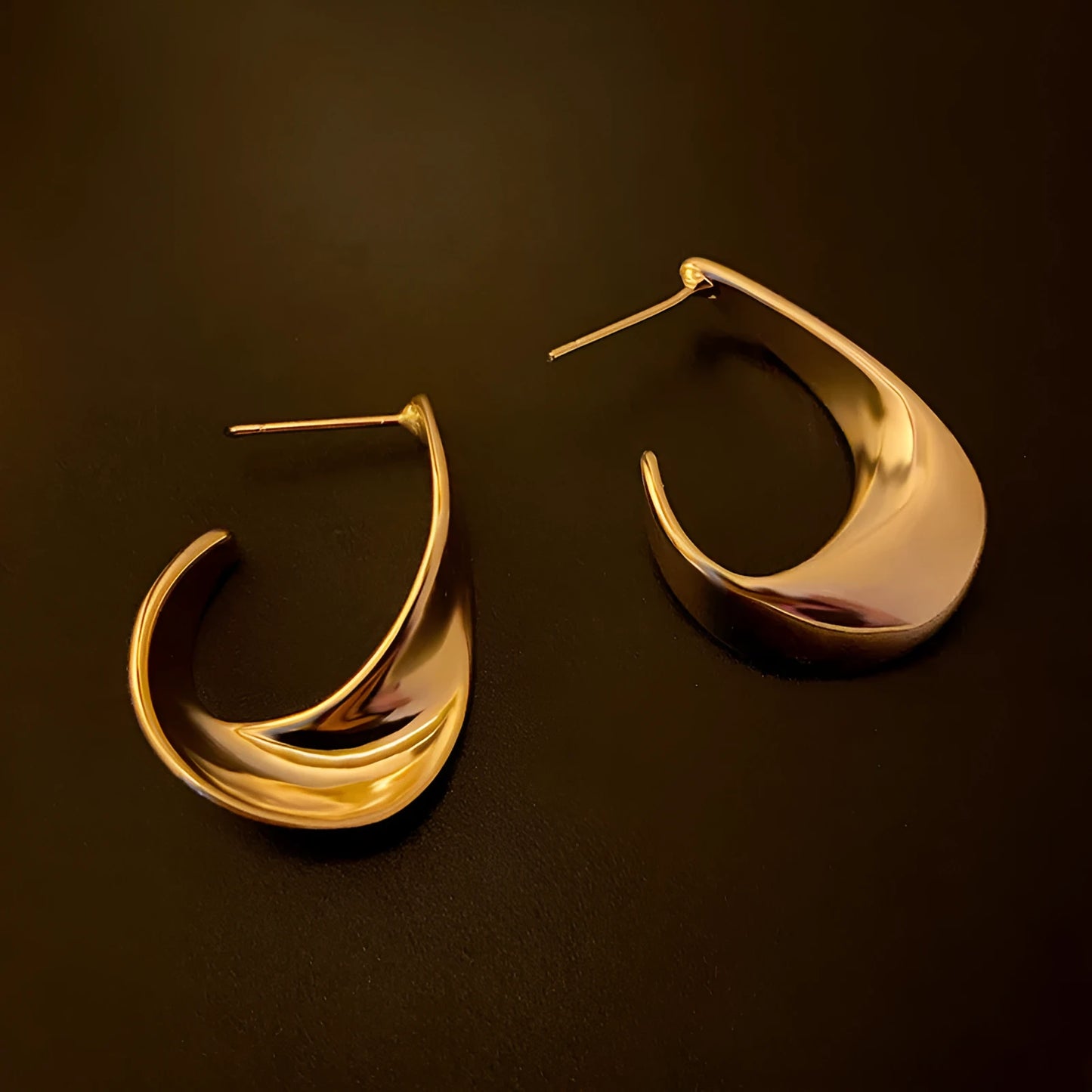 A pair of gold twisted geometric metal earrings with a round detail on a white background.