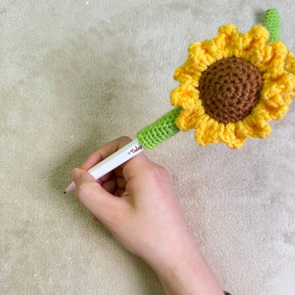 Hand-woven yellow and brown sunflower pen cover holding a pen.