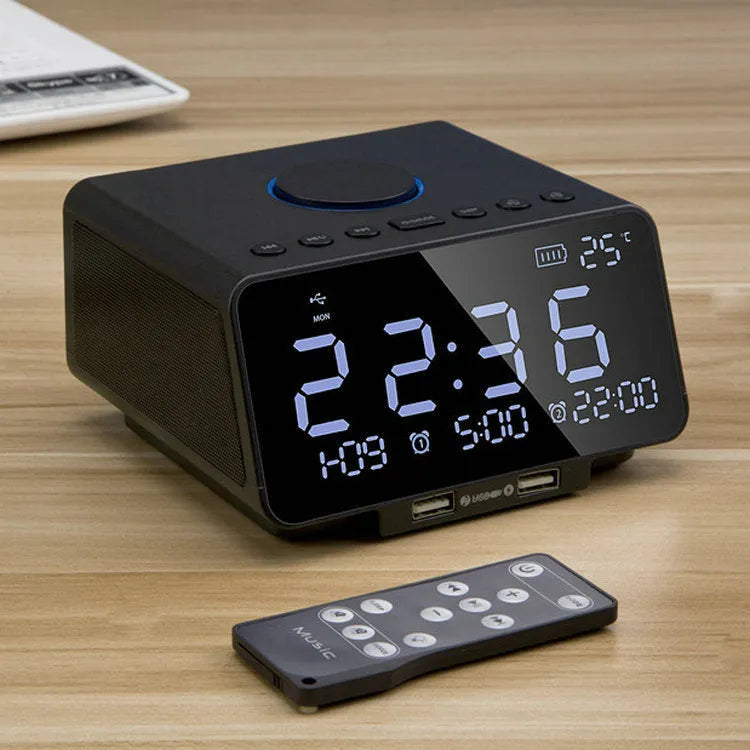 Black and white wireless alarm clock Bluetooth speaker with remote control on a table.