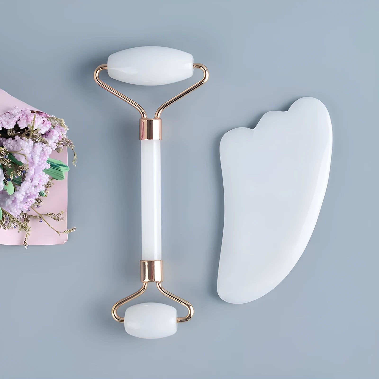 White jade facial roller with double-headed claw design and matching scraping board on dark surface