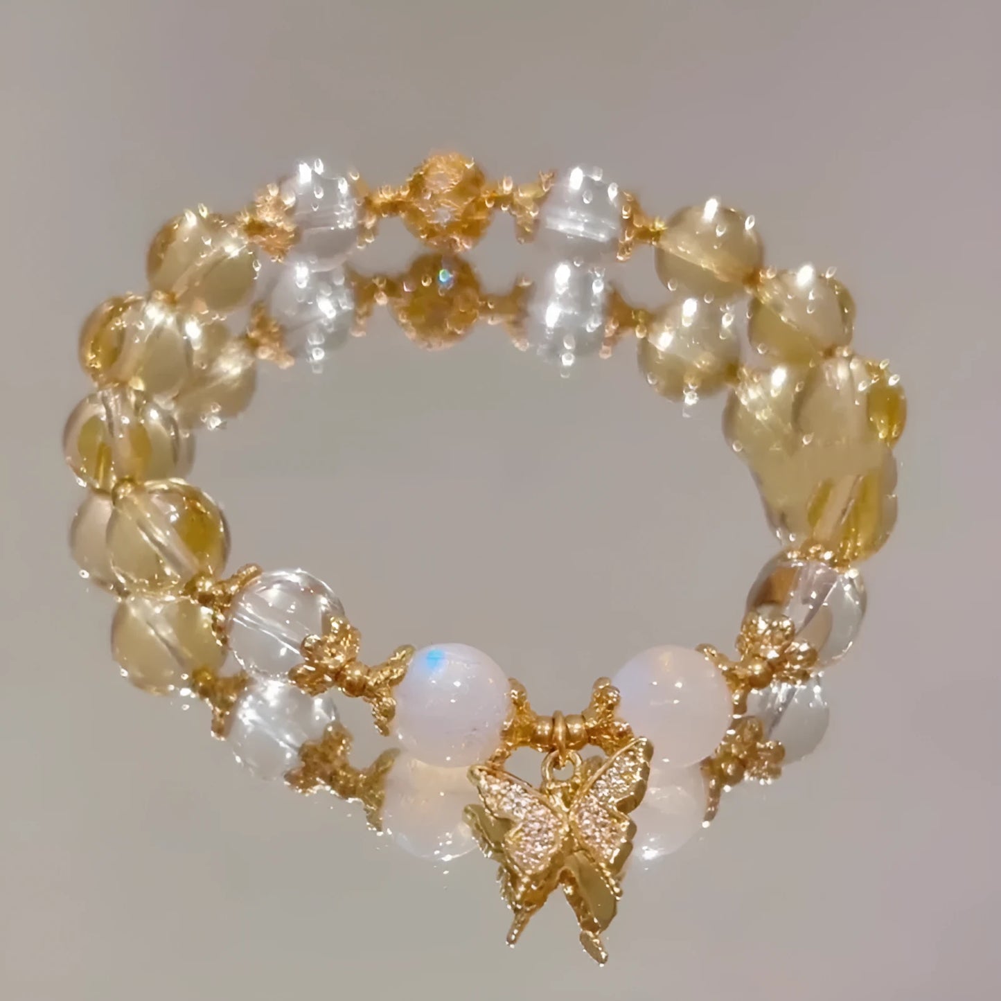 Close-up of a citrine-coloured crystal bracelet with diamond-shaped beads and a butterfly charm.