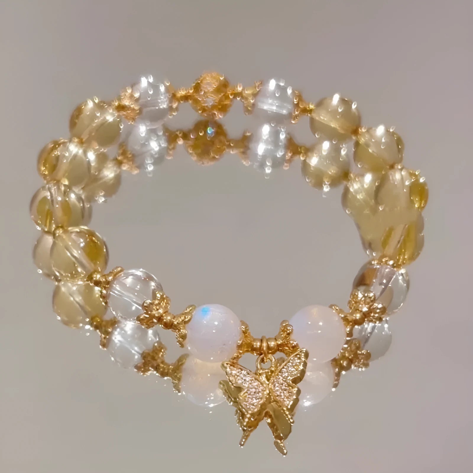 Close-up of a citrine-coloured crystal bracelet with diamond-shaped beads and a butterfly charm.