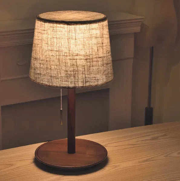 Walnut coloured solid wood bedside lamp with white fabric shade and cable switch.