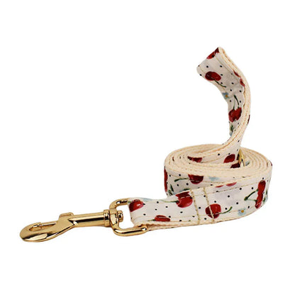 Red cherry printed dog collar with light gold buckle and matching leash, bow, vest and poop bag holder set