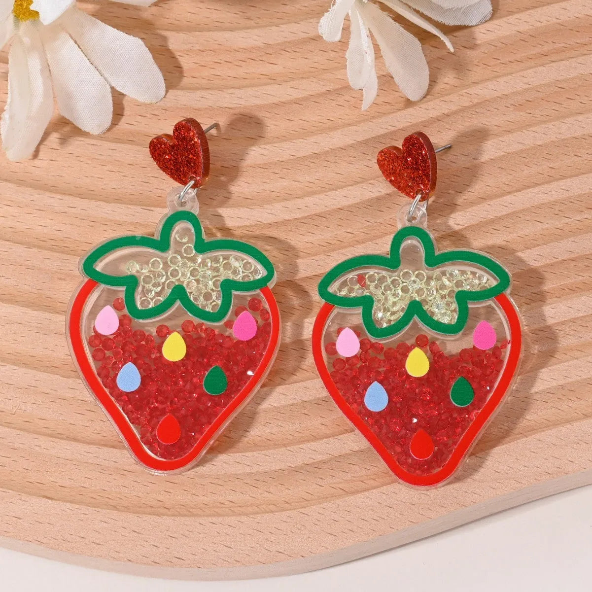 A pair of colourful acrylic earrings shaped like a strawberry and a cherry on a woman's ear.