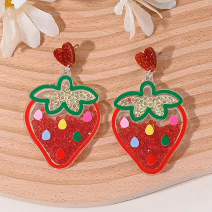 A pair of colourful acrylic earrings shaped like a strawberry and a cherry on a woman's ear.