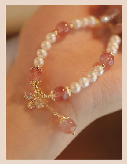 Women's strawberry quartz crystal bracelet with a decorative bow charm on a wrist.