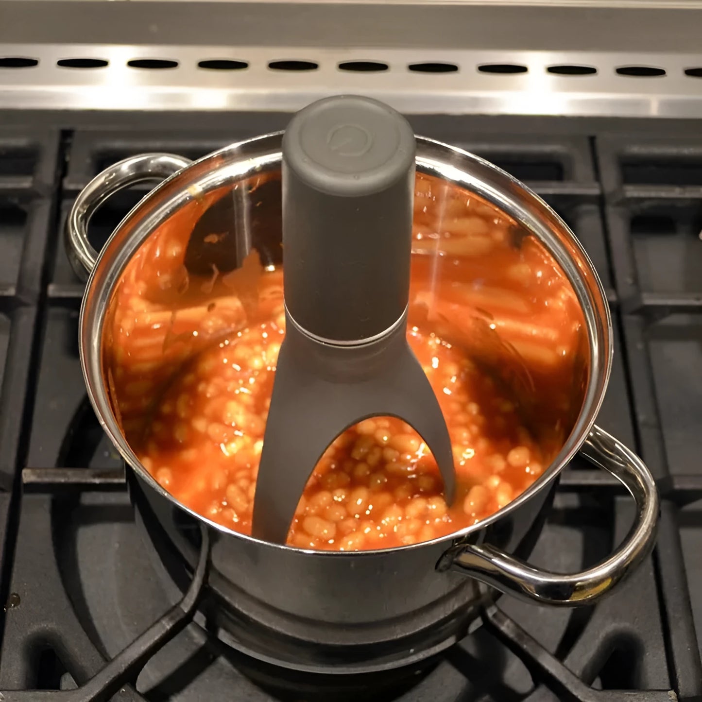 Uutensil Stirr automatic cooking mixer in grey, shown stirring in a pot of sauce.