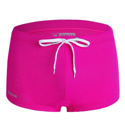 Men's low waist swim trunks in stretch nylon on a man, showing elastic waistband and boxer-style cut.