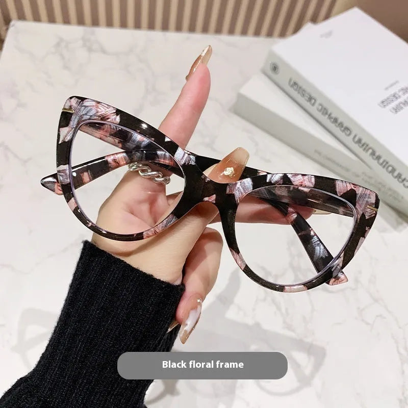Women's black floral cat's eye reading glasses with large frames on a wooden table.
