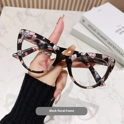 Women's black floral cat's eye reading glasses with large frames on a wooden table.