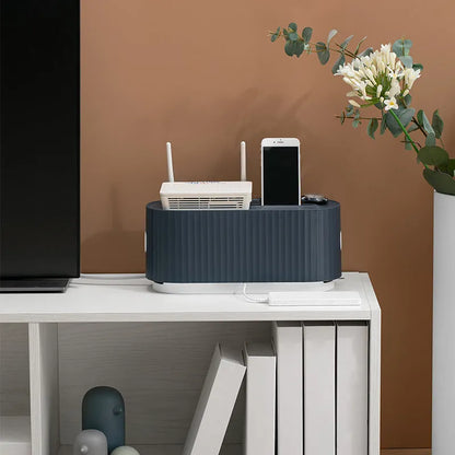 Blue desktop cable storage box with a white lid, showing cable ports on the base and a mobile phone sitting in its slot on top.