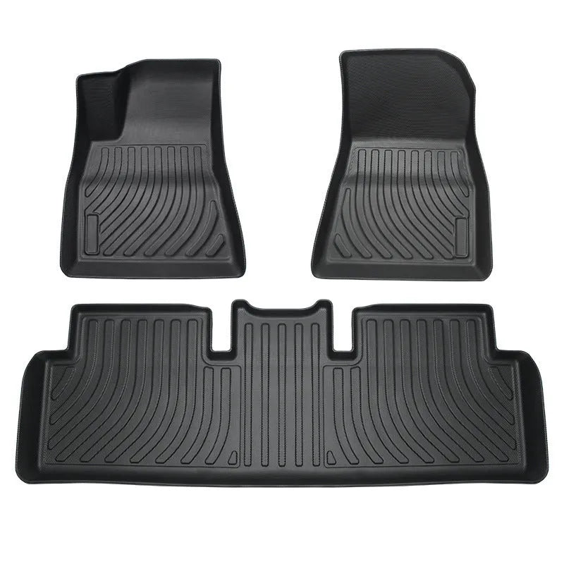 Custom black rubber floor mats fitted in a Tesla Model 3, showing deep grooves and raised edges.